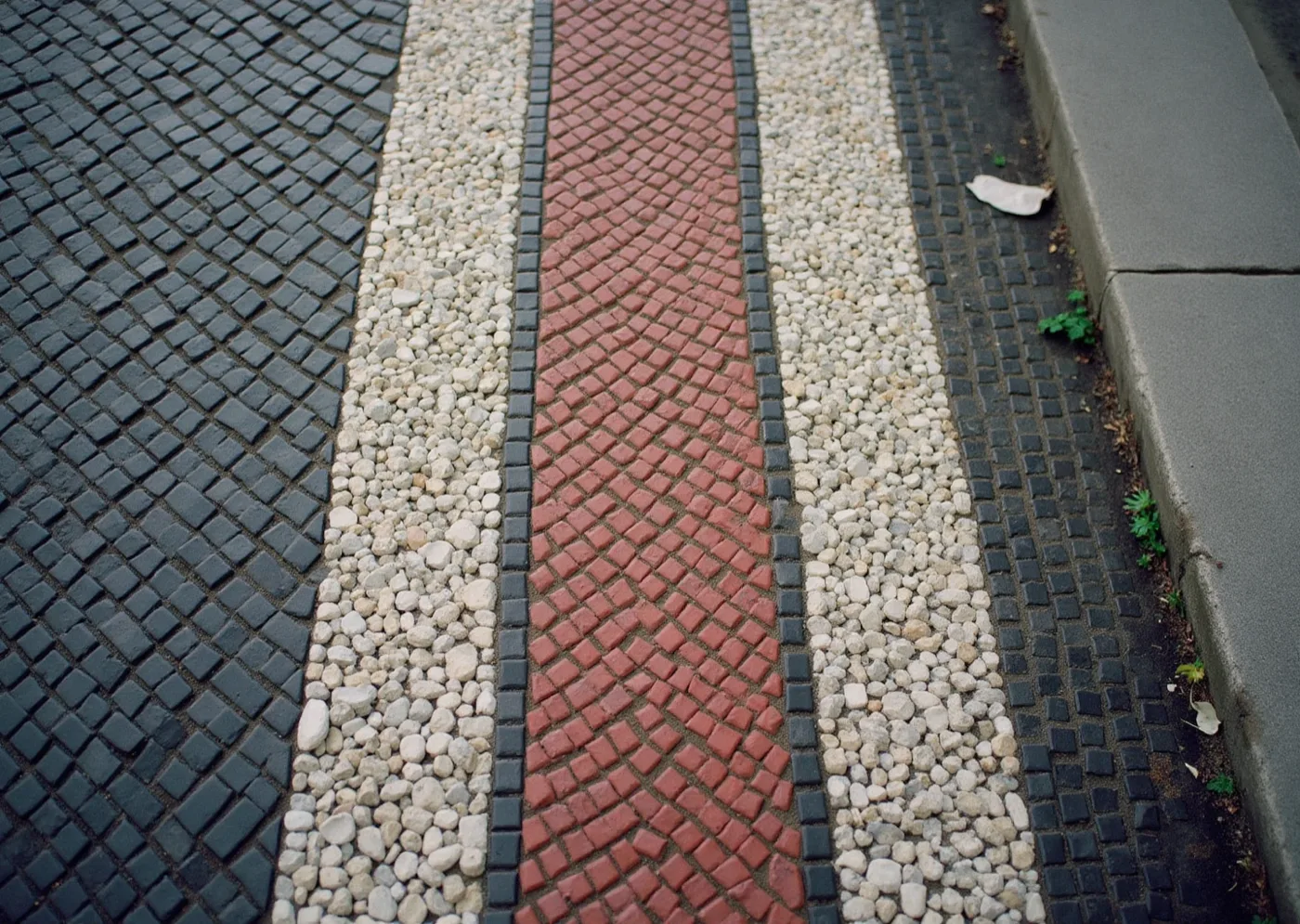 Modernist mosaic pavement seen from directly above — small stones laid in a bold curving pattern, worn smooth, with one section visibly repaired.