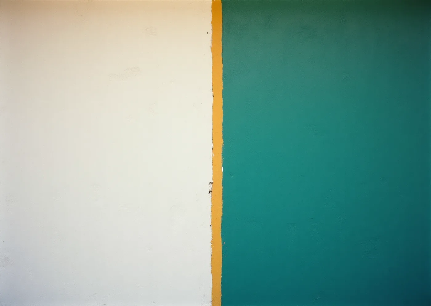 A single saturated painted wall at the hottest hour of the day, half of it blown out in direct sun and half dense in deep shade, with a hard diagonal between the two.