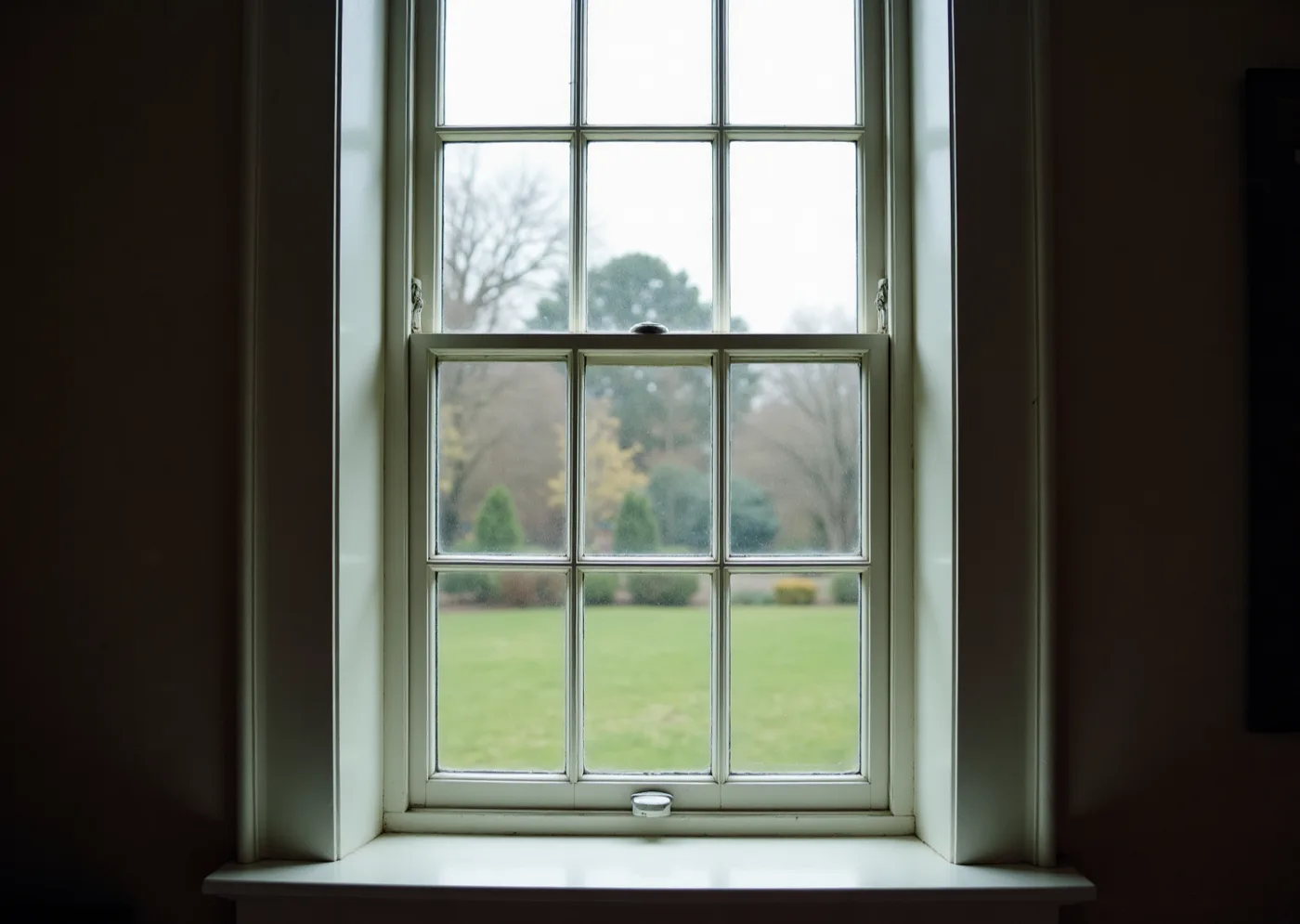 A tall multi-pane sash window seen square-on from inside, its glazing bars forming a strict grid, daylight flat across the panes.